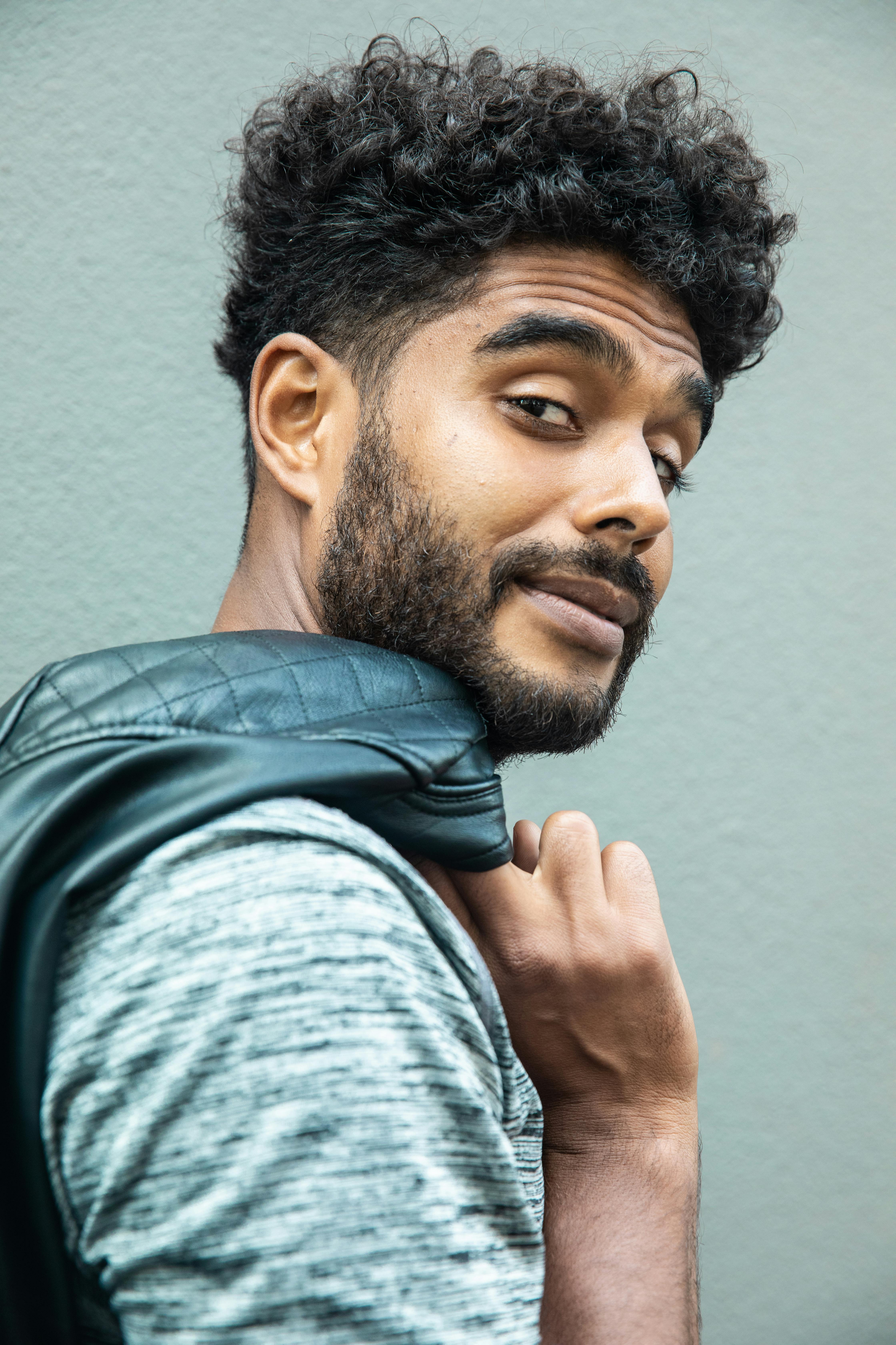 Stylish young man with curly hair and beard looking confidently over his shoulder.