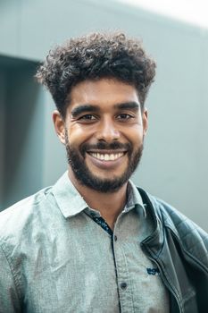 Portrait of a happy young man with curly hair and a beaming smile, wearing a leather jacket outdoors.