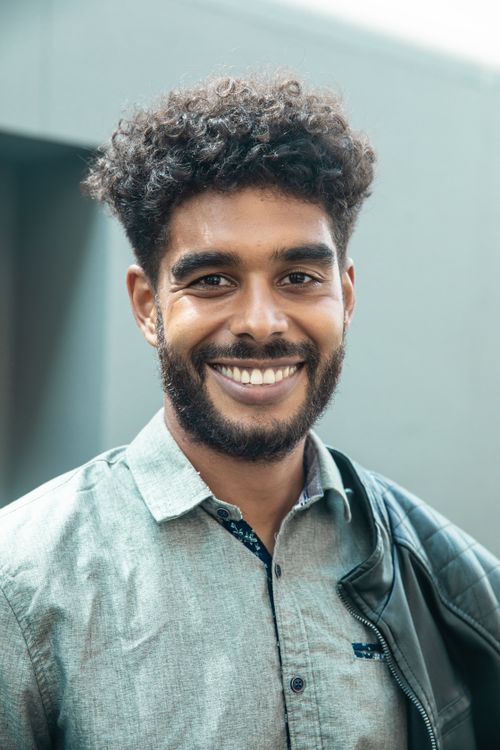 Free Portrait of a happy young man with curly hair and a beaming smile, wearing a leather jacket outdoors. Stock Photo