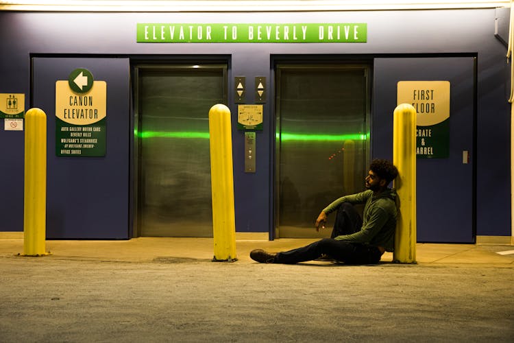 Man Sitting On Ground Near An Elevator Lobby