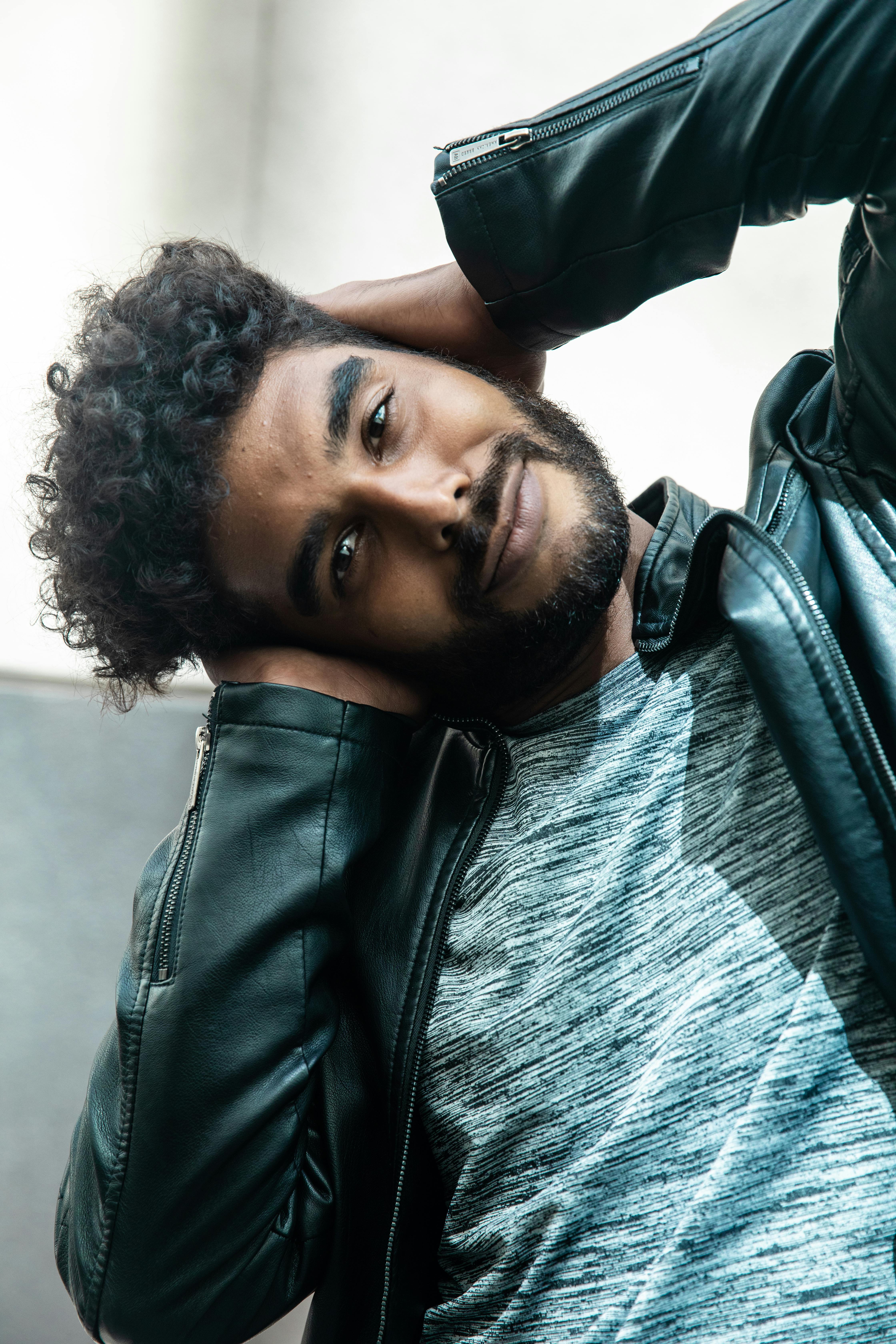 Casual portrait of a confident man in a black leather jacket covering ears, looking at the camera.