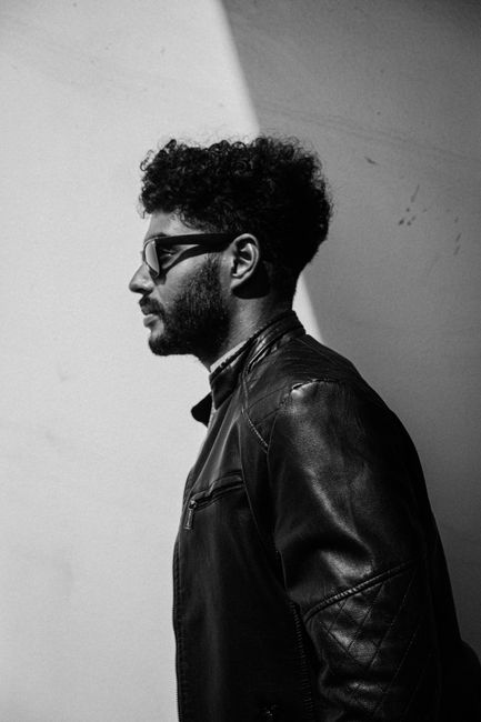 Black and white portrait of a stylish man in profile wearing a leather jacket and sunglasses.