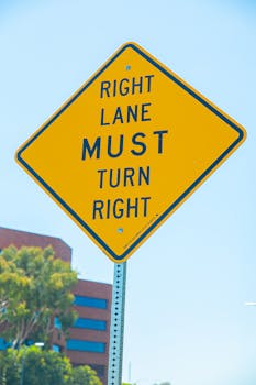 Yellow diamond traffic sign indicating right lane must turn right in urban setting.
