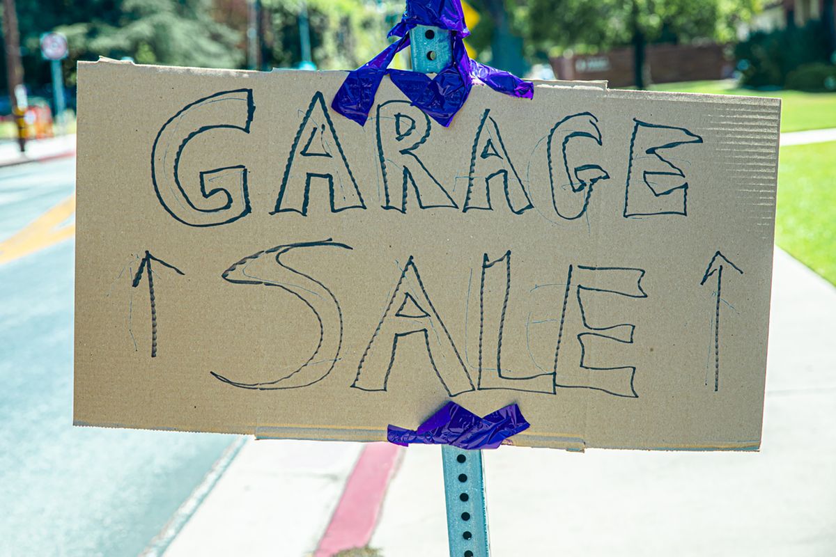 Handwritten cardboard garage sale sign with arrows taped to a street post, advertising a moving sale
