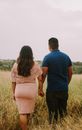 Back view of anonymous boyfriend in blue shirt and jeans and faceless girlfriend in pink lace dress holding hands while walking in meadow