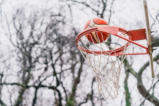 Close-up of a basketball scoring through a hoop on an outdoor court in winter.