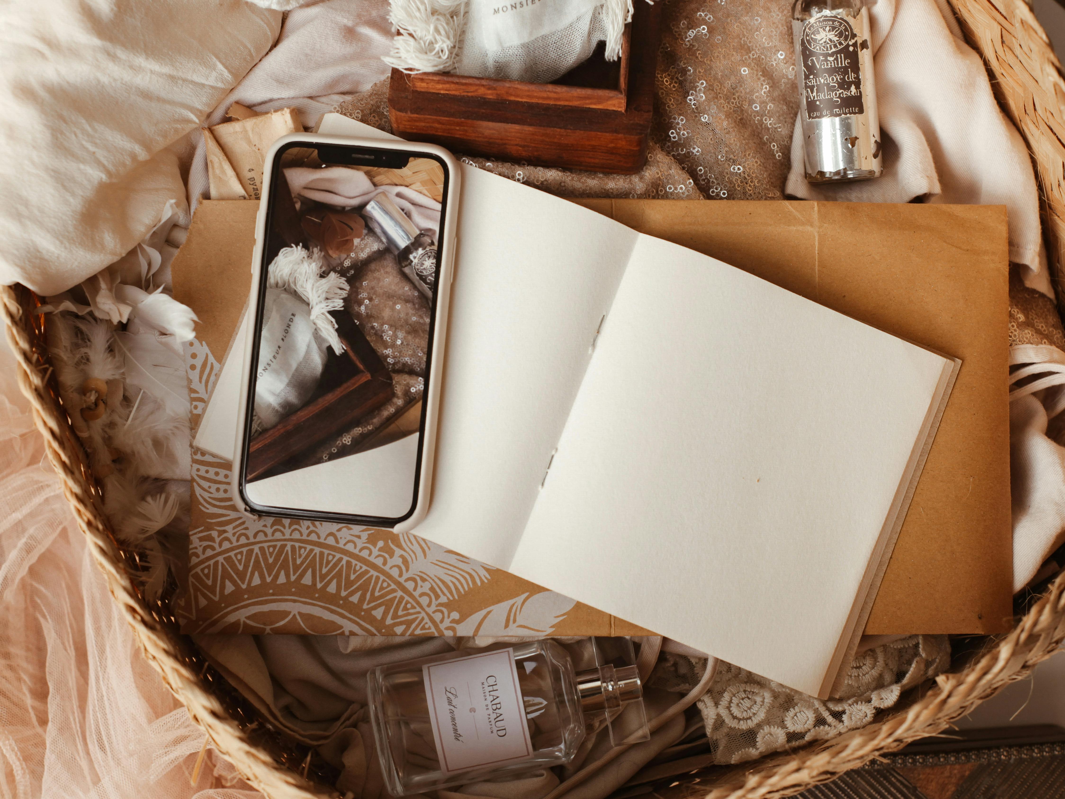 编织篮子里，一台打开的笔记本电脑、一部智能手机和一瓶香水错落有致地摆放着，充满艺术气息