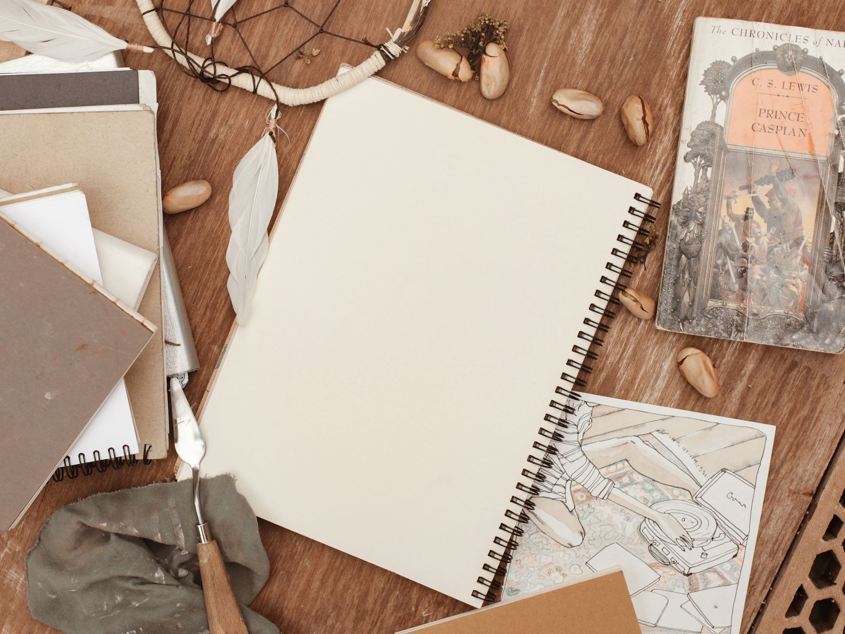 Flat lay of a sketchbook surrounded by artistic tools and a novel for creative inspiration.
