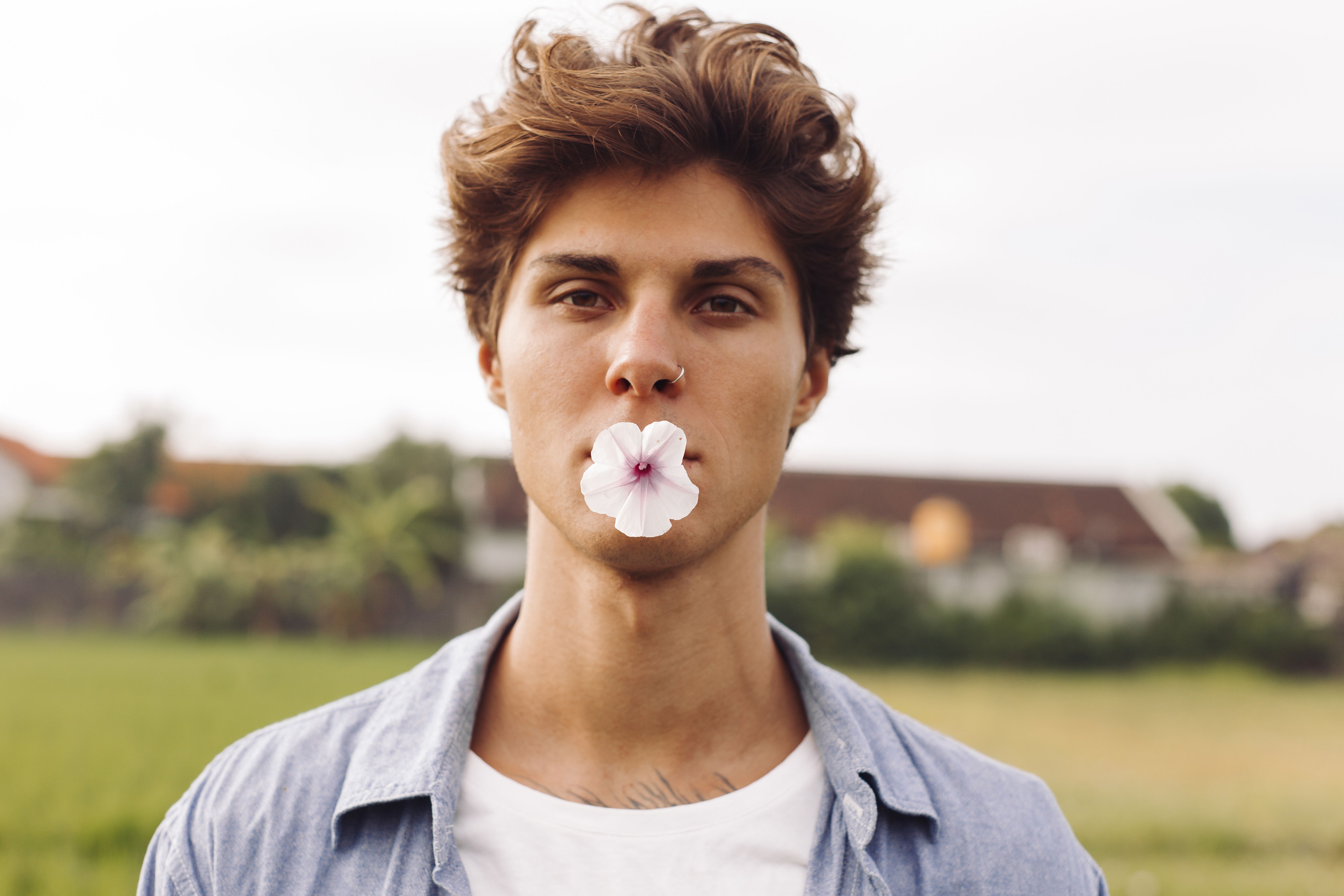 一个男人站在户外，嘴里叼着一朵花的特写镜头