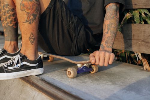 Free Close-up of a tattooed skater sitting on a skateboard outdoors, showcasing unique tattoos and skate style. Stock Photo