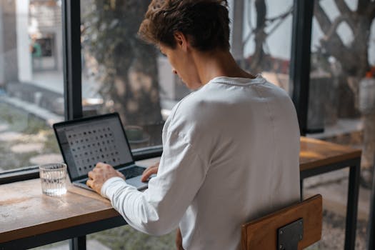 Young man using a laptop in a cozy indoor setting with natural light.