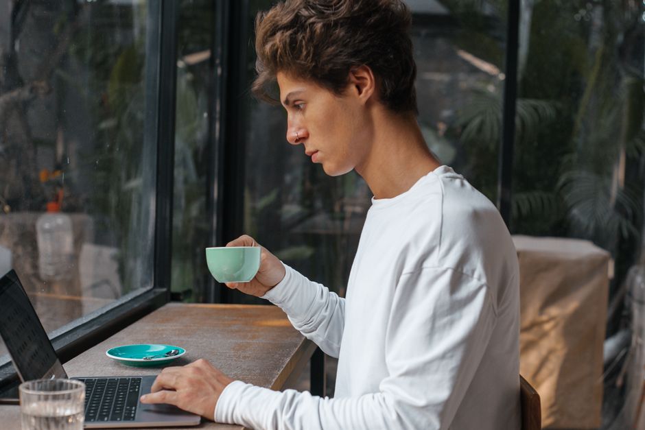 Young man focused on laptop while enjoying coffee in a cozy café setting. Young man focused on laptop while enjoying coffee in a cozy café setting.