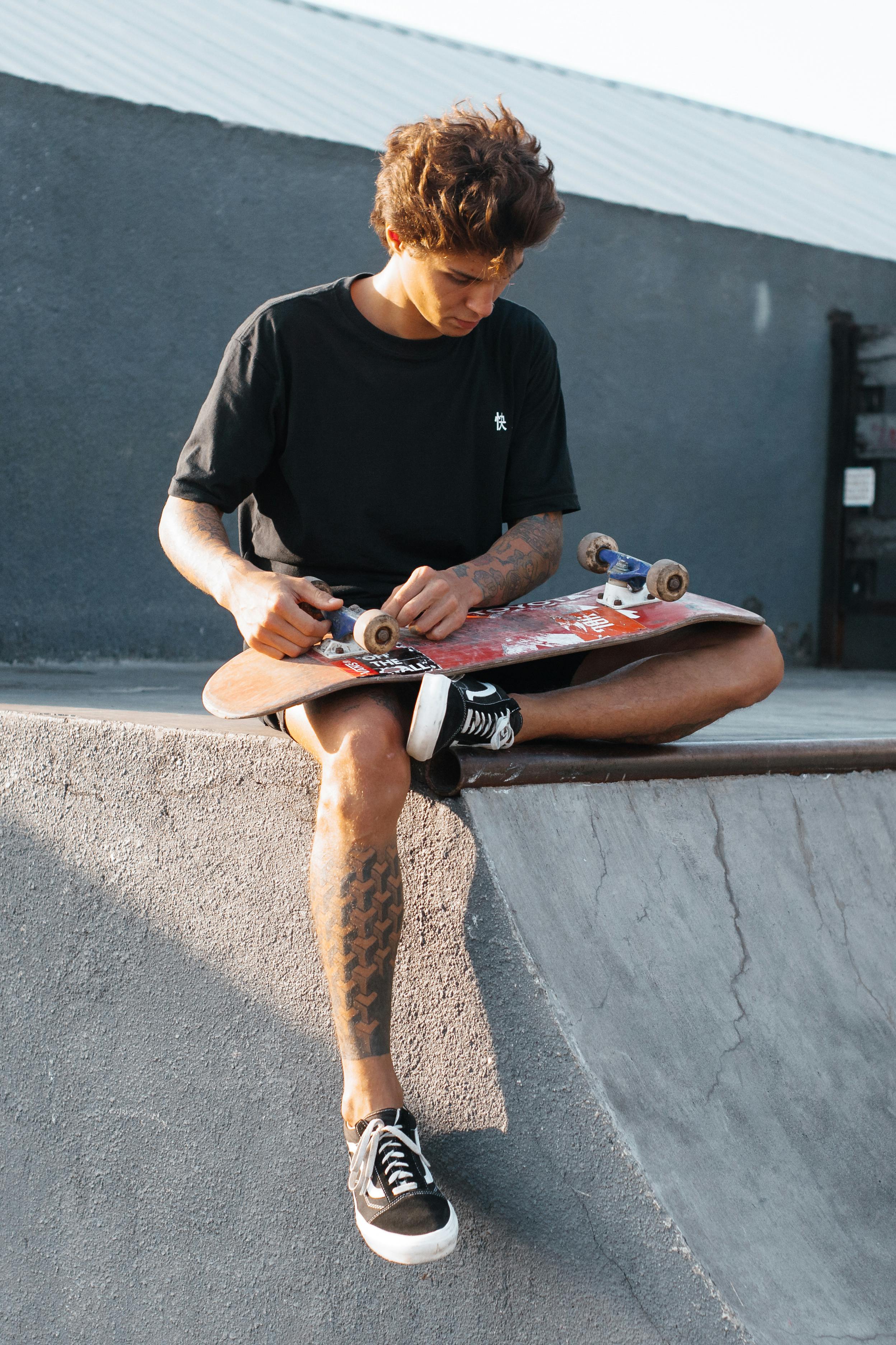 Young man sitting on a ramp tuning his skateboard under the sun.