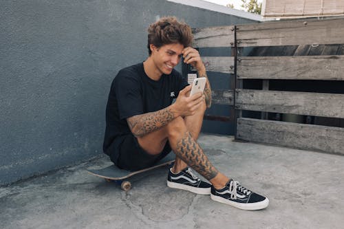 Man in Black Shirt Sitting on Skateboard While Using a Cellphone