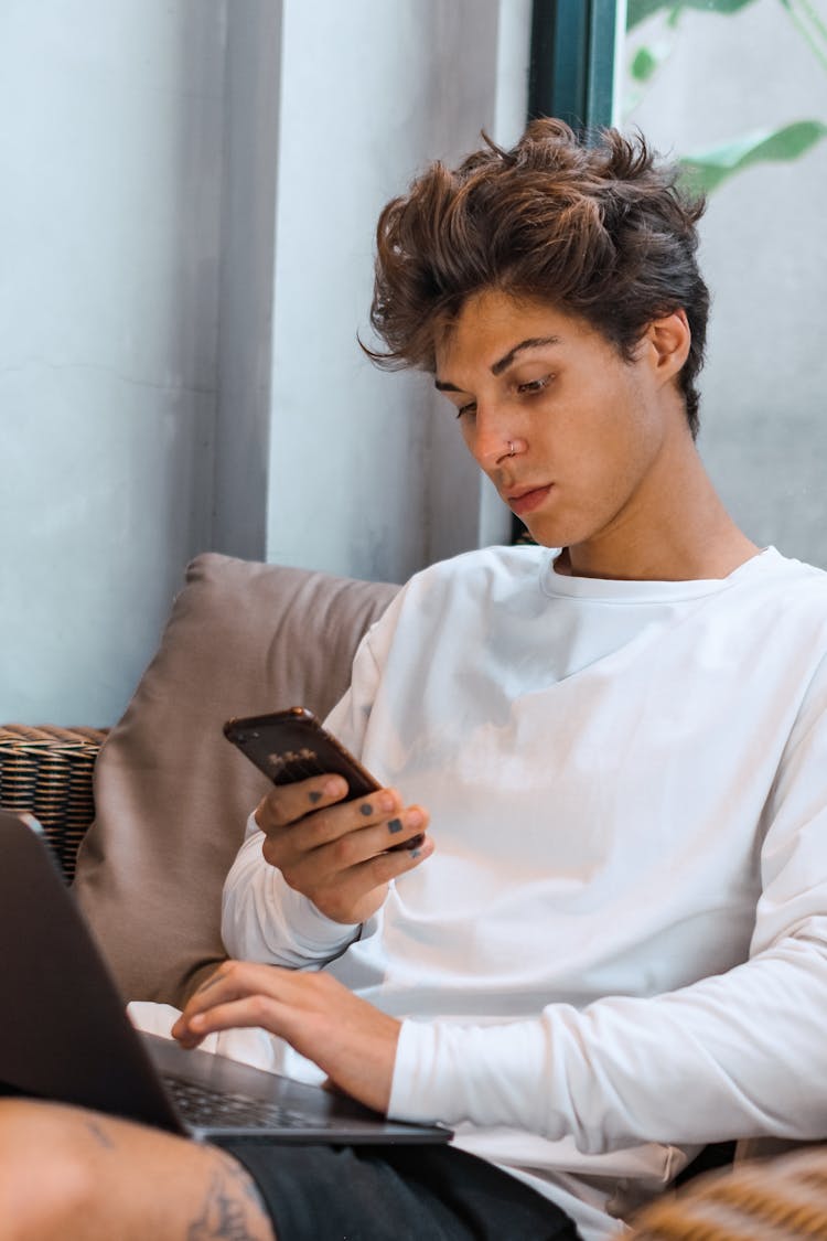 Man In White Top Using Mobile Phone And Laptop Computer