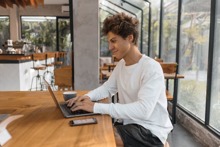 Young Man Working On A Laptop In A Cafe 