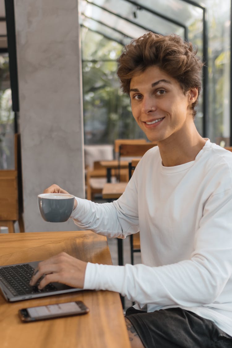 Young Man Using Laptop And Drinking Coffee In A Cafe 