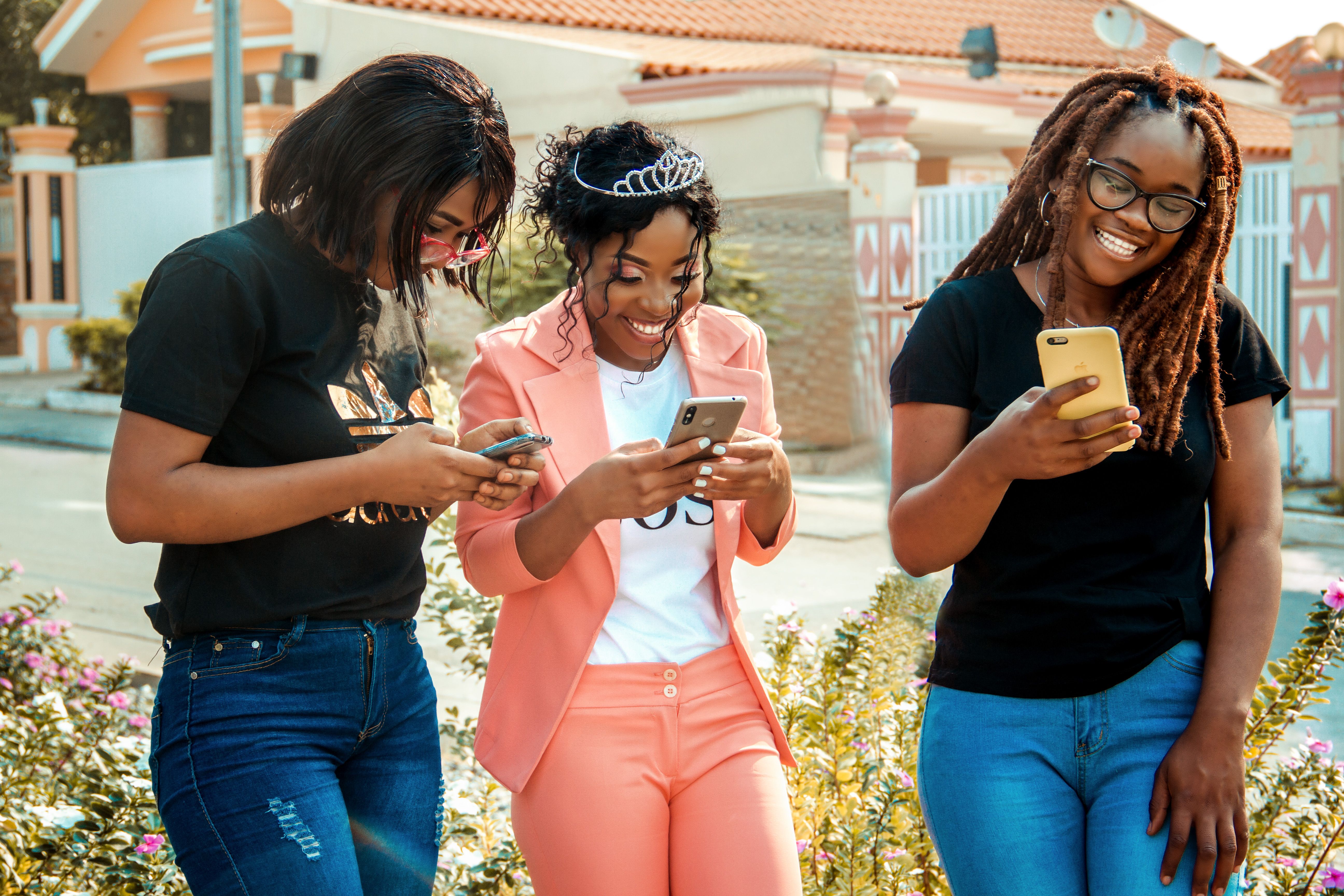 Happy ethnic women in trendy wear text messaging on cellphones on city street