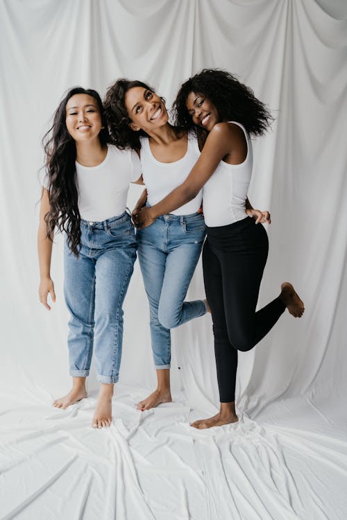 2 Wanita Dengan Tank Top Putih Dan Jeans Denim Biru Berdiri Di Atas Tekstil Putih