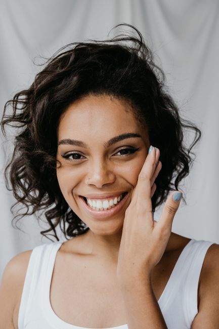 A cheerful woman with curly hair and a radiant smile in a close-up portrait indoors.