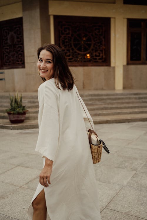 A Woman in White Dress Smiling while Carrying a Sling Bag