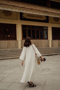 一名身穿白色连衣裙的女子走向越南寺庙，展示着传统建筑
