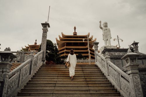 Free A woman in a white dress climbs stairs towards an ornate buddhist temple with large sculptures. Stock Photo