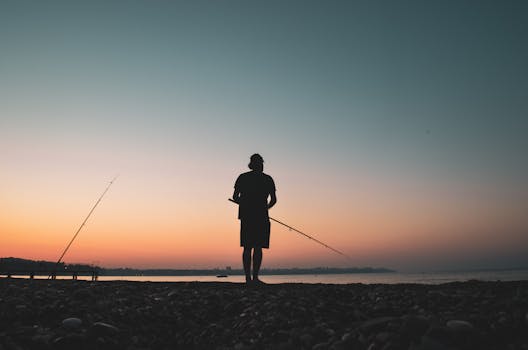 Serene silhouette of a man fishing at the seashore during a beautiful sunset with a pink sky.