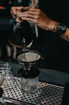Close-up of hands preparing pour over coffee with precision in a cozy cafe.