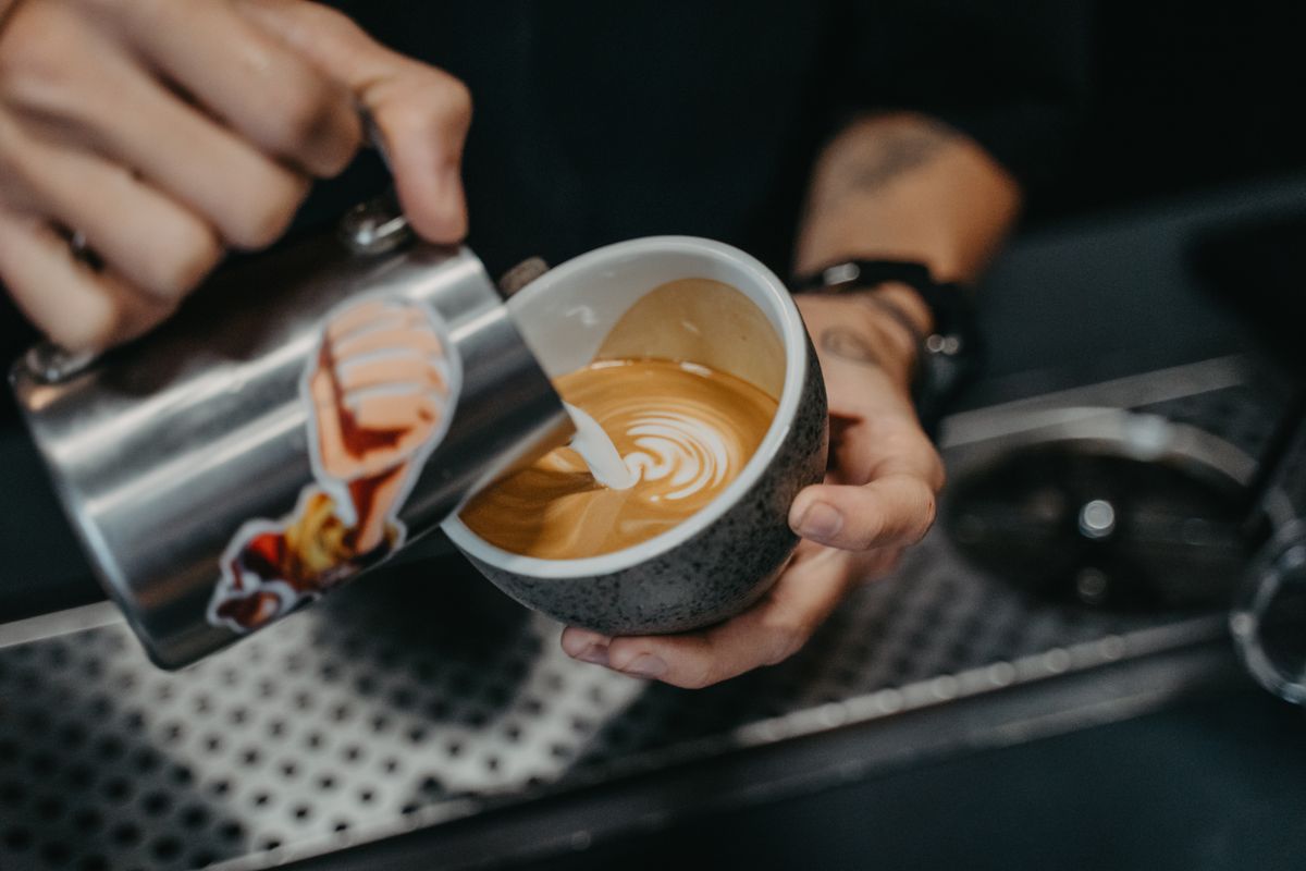 A Brewline barista pouring latte art into a ceramic cup.