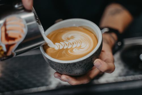 Free Close-up of a barista pouring milk to create intricate latte art in a ceramic cup. Stock Photo