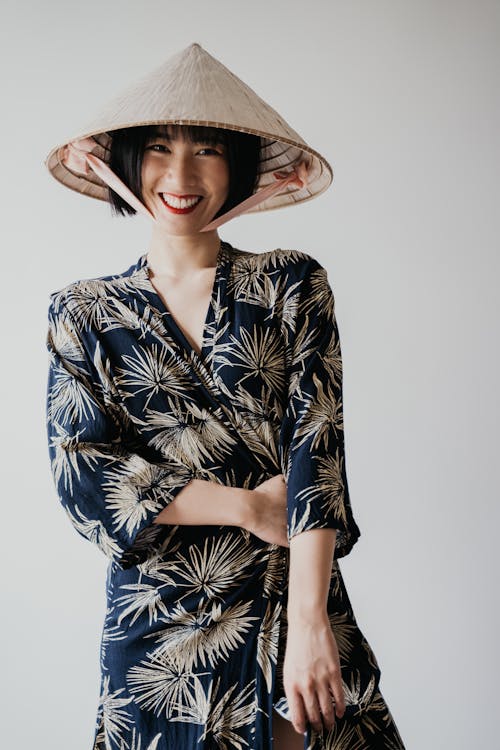 A Woman in a Blue Printed Dress Smiling while Wearing a Rice Hat