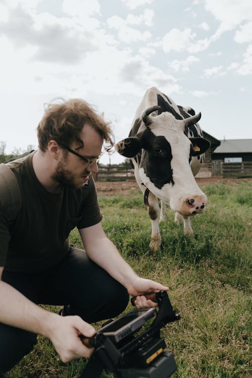 Man in Black Crew Neck T-shirt Sitting Beside Cow