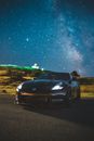 Modern coupe car with glowing headlights parked on asphalt road against bright night sky