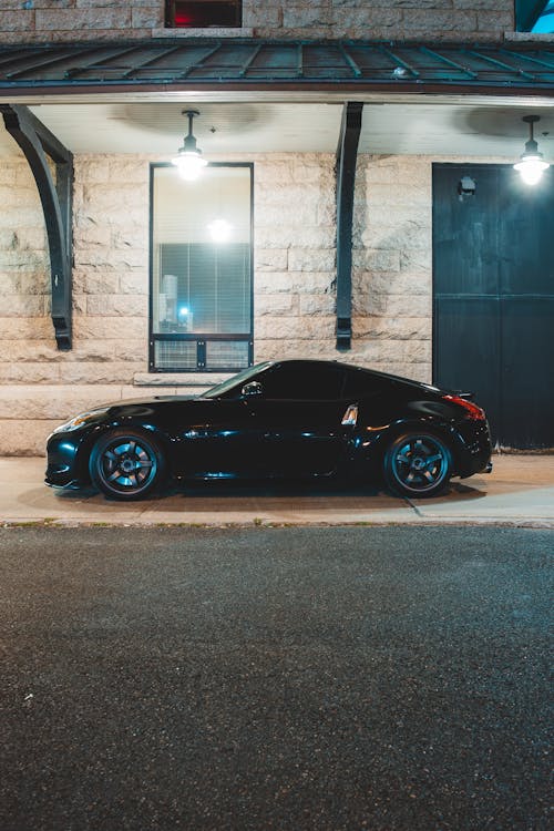 Prestigious coupe car parked under canopy of building with stone wall and big window