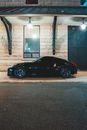 Prestigious coupe car parked under canopy of building with stone wall and big window