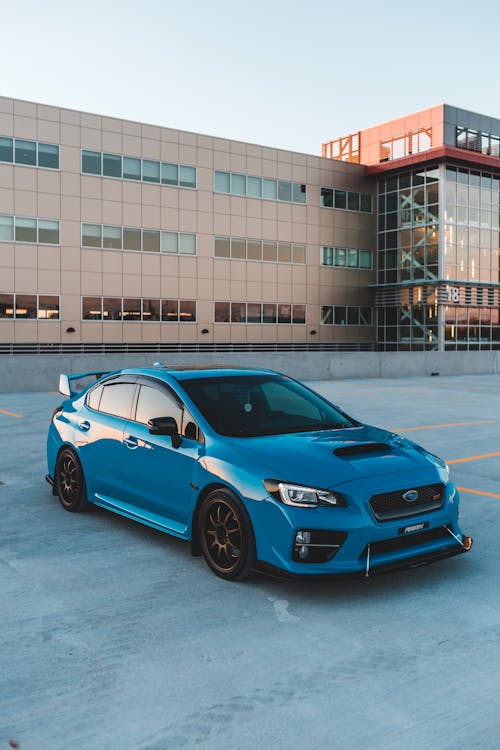 Exterior of coupe blue car parked on asphalt parking outside modern building in early evening