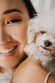一位微笑的年轻亚洲女子与她的白色狮子狗同伴拥抱的特写照