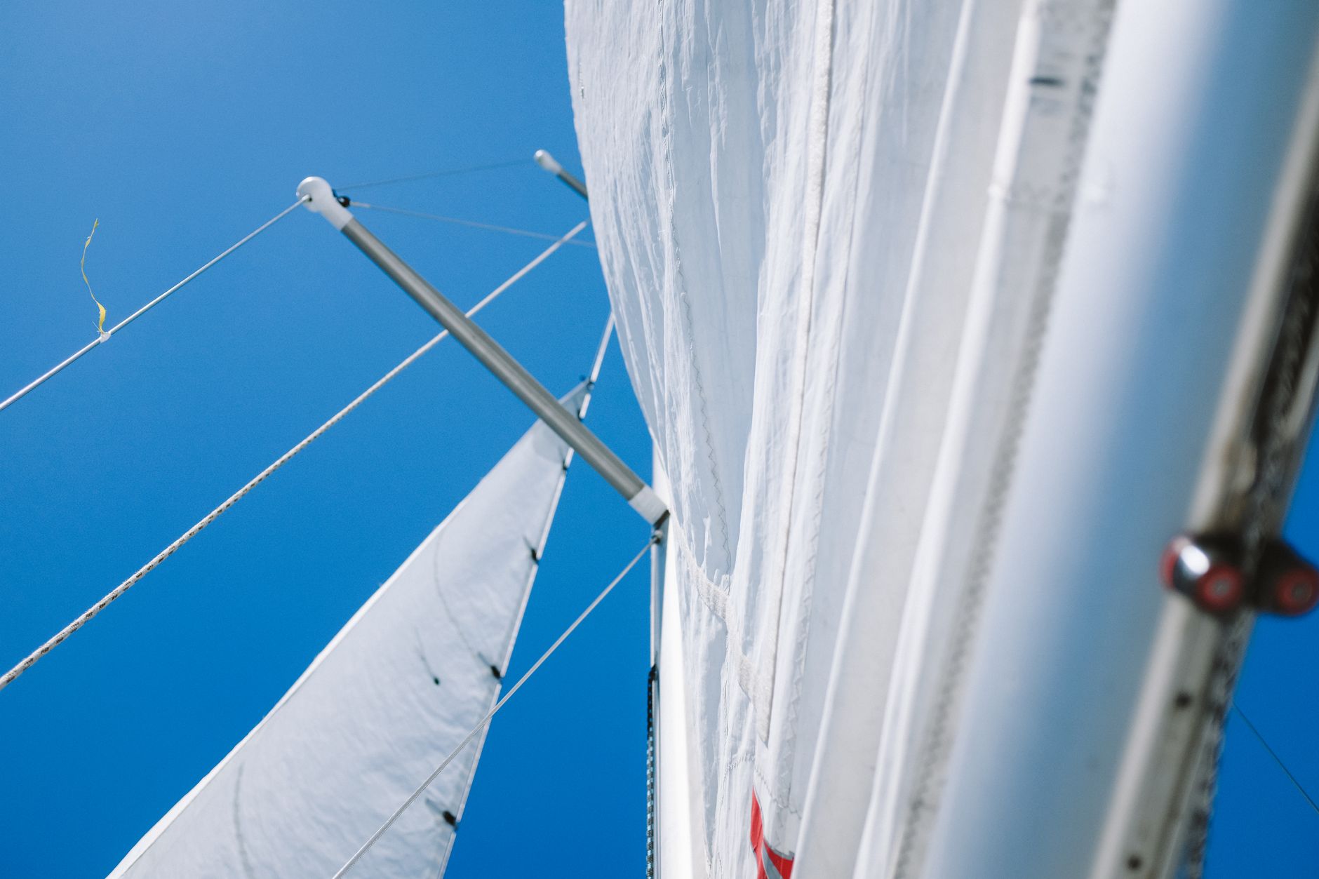 Close-up view of a sailboat mast and sails against a clear blue sky, highlighting nautical adventure.