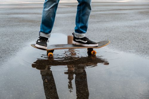 Free A skateboarder's legs reflected in a puddle while balancing on a skateboard. Stock Photo
