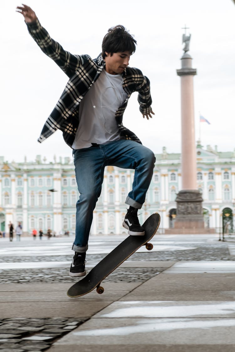 Man In Black And White Plaid Dress Shirt And Blue Denim Jeans Sitting On Black Skateboard