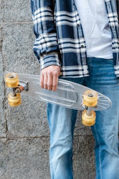 Close-up of a man in casual attire holding a transparent skateboard against a granite wall.
