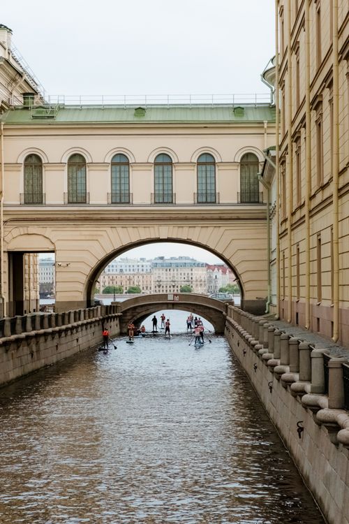 Free Standup paddleboarders navigate a canal under a historic archway in Saint Petersburg. Stock Photo