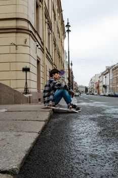 一位年轻的滑板运动员坐在圣彼得堡一条历史悠久的街道上沉思