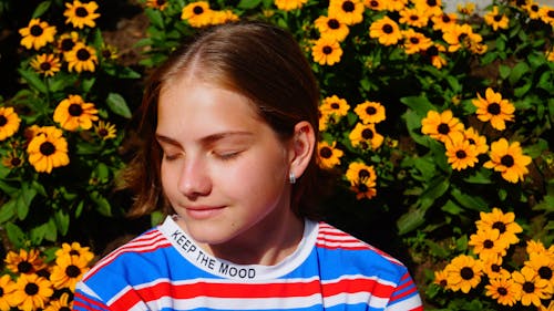 Girl in Striped T-Shirt with Eyes Closed Sitting Beside Yellow Flowers