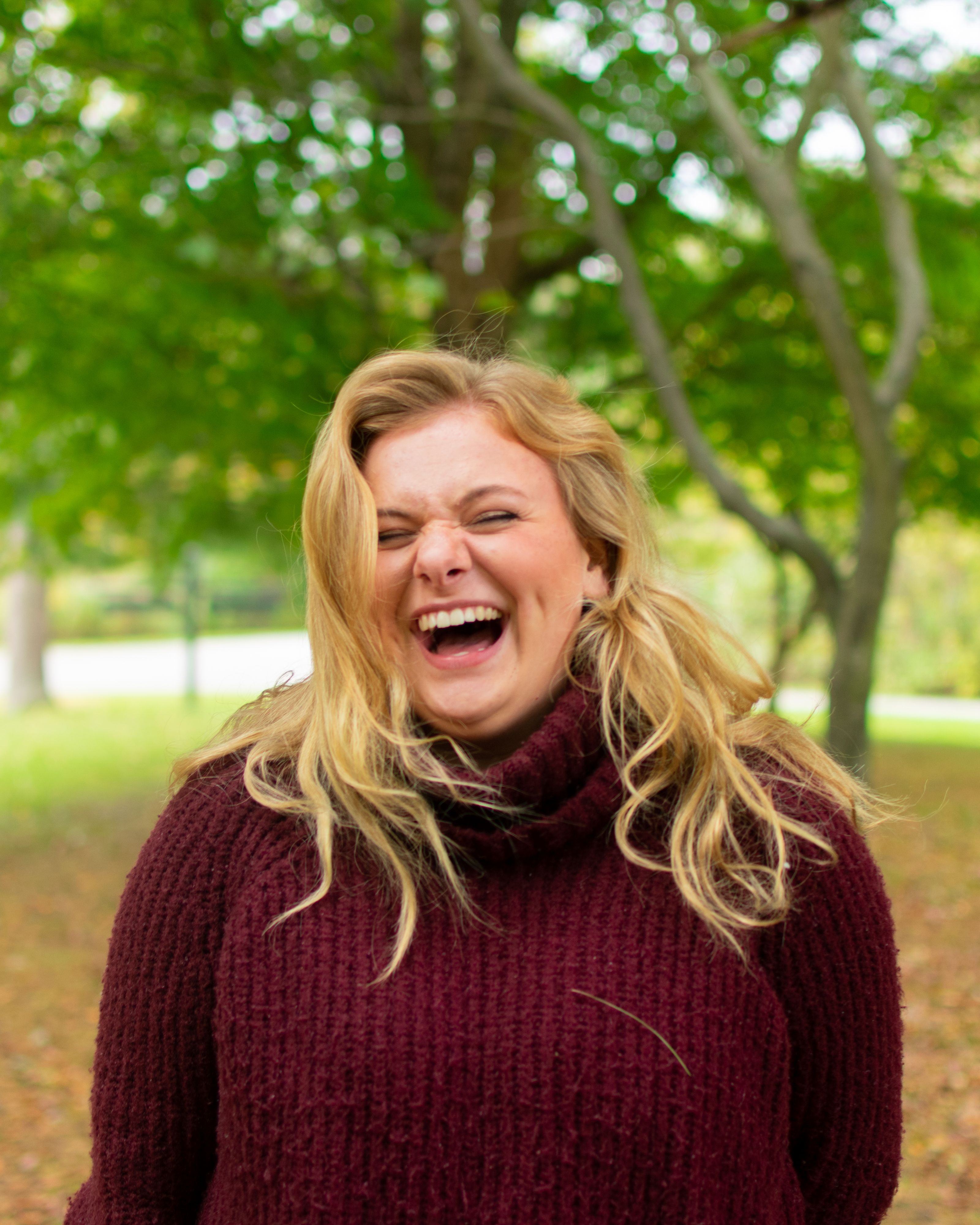 Smiling woman in a sweater enjoying a laugh during a sunny autumn day outdoors.