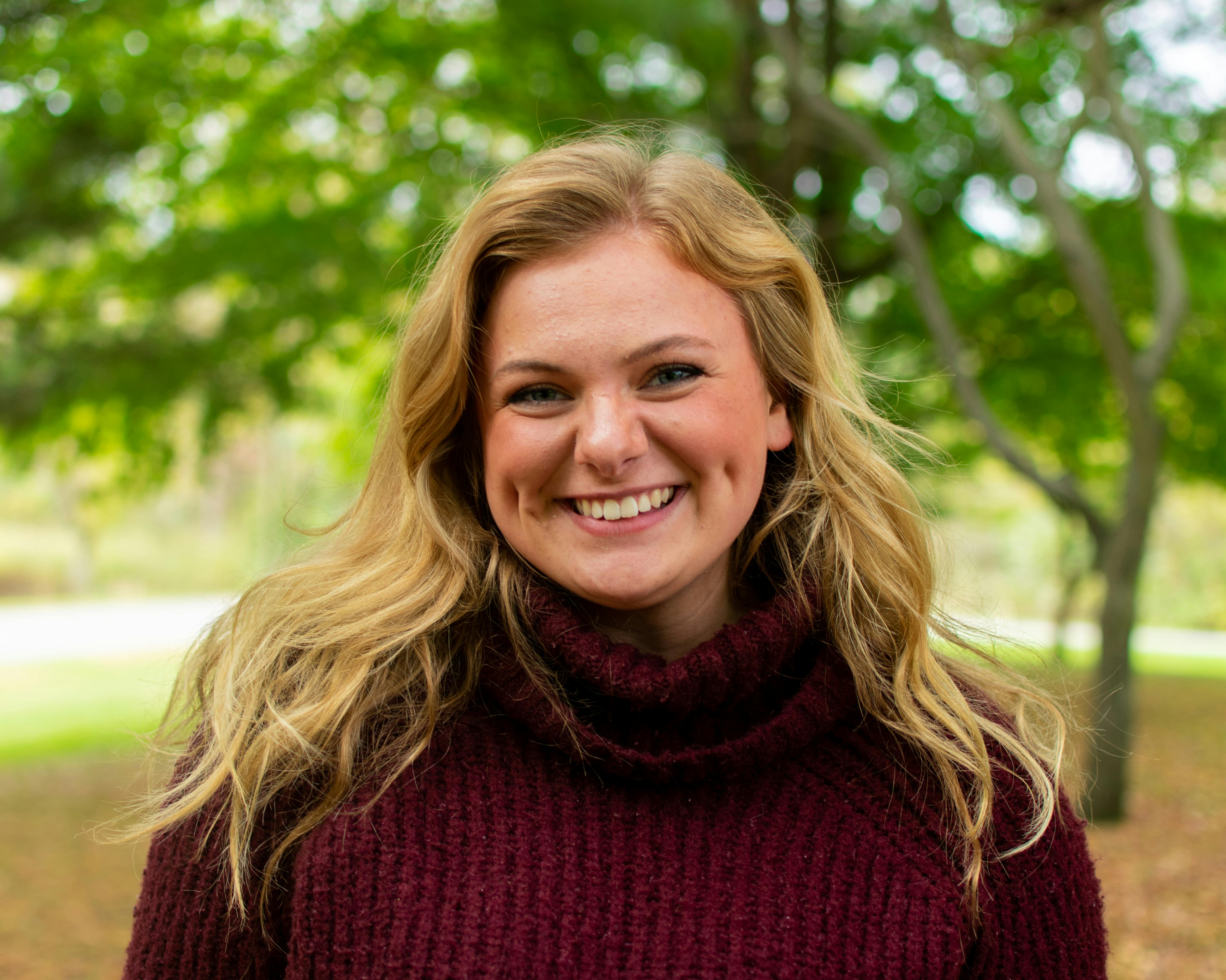 Portrait of a smiling woman with blond hair in an autumn outdoor setting.