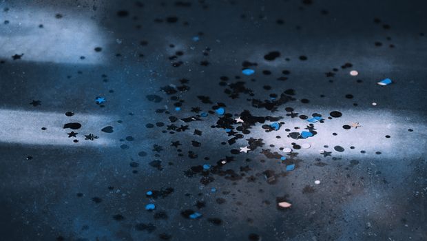 A close-up of colorful confetti scattered on a dark, textured floor.