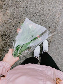 Top view of anonymous person in casual clothes and white sneakers holding bouquet of flowers and standing on asphalt
