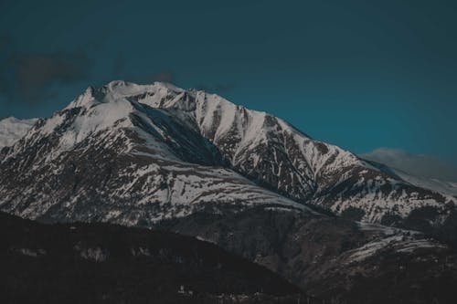 Amazing landscape of huge mountain range covered with snow against cloudy blue sky in evening